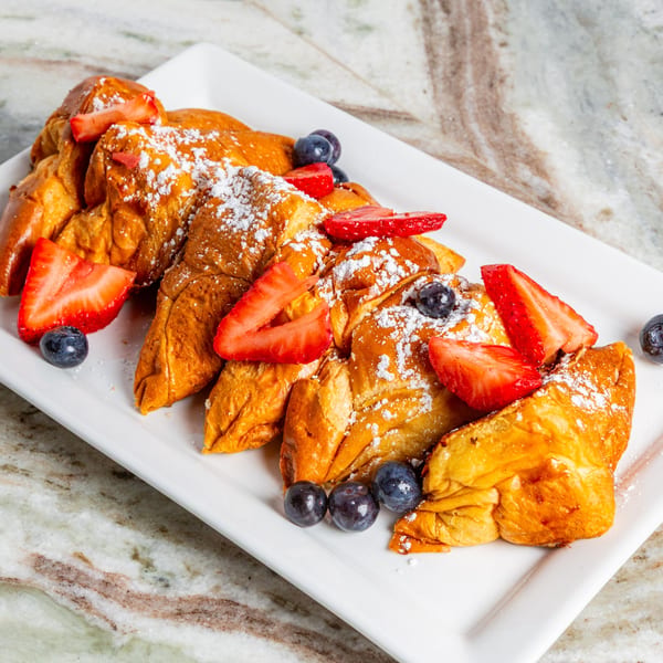 Golden-brown French toast triangles, dusted with powdered sugar, topped with fresh strawberries and blueberries.