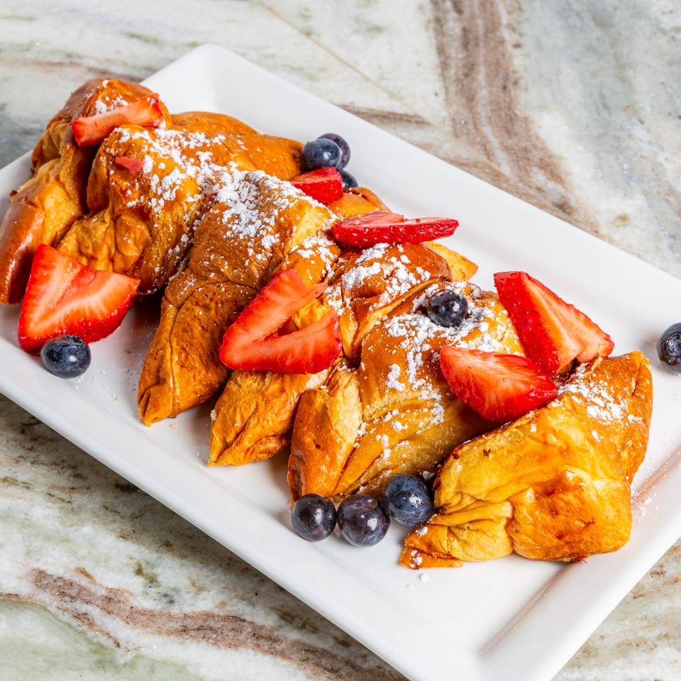Golden-brown French toast triangles, dusted with powdered sugar, topped with fresh strawberries and blueberries.