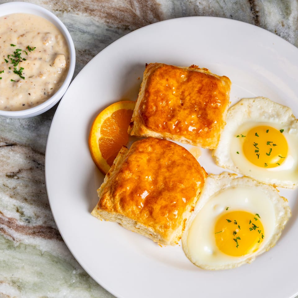 Southern breakfast with biscuits, two fried eggs, an orange slice, and a side of gravy.