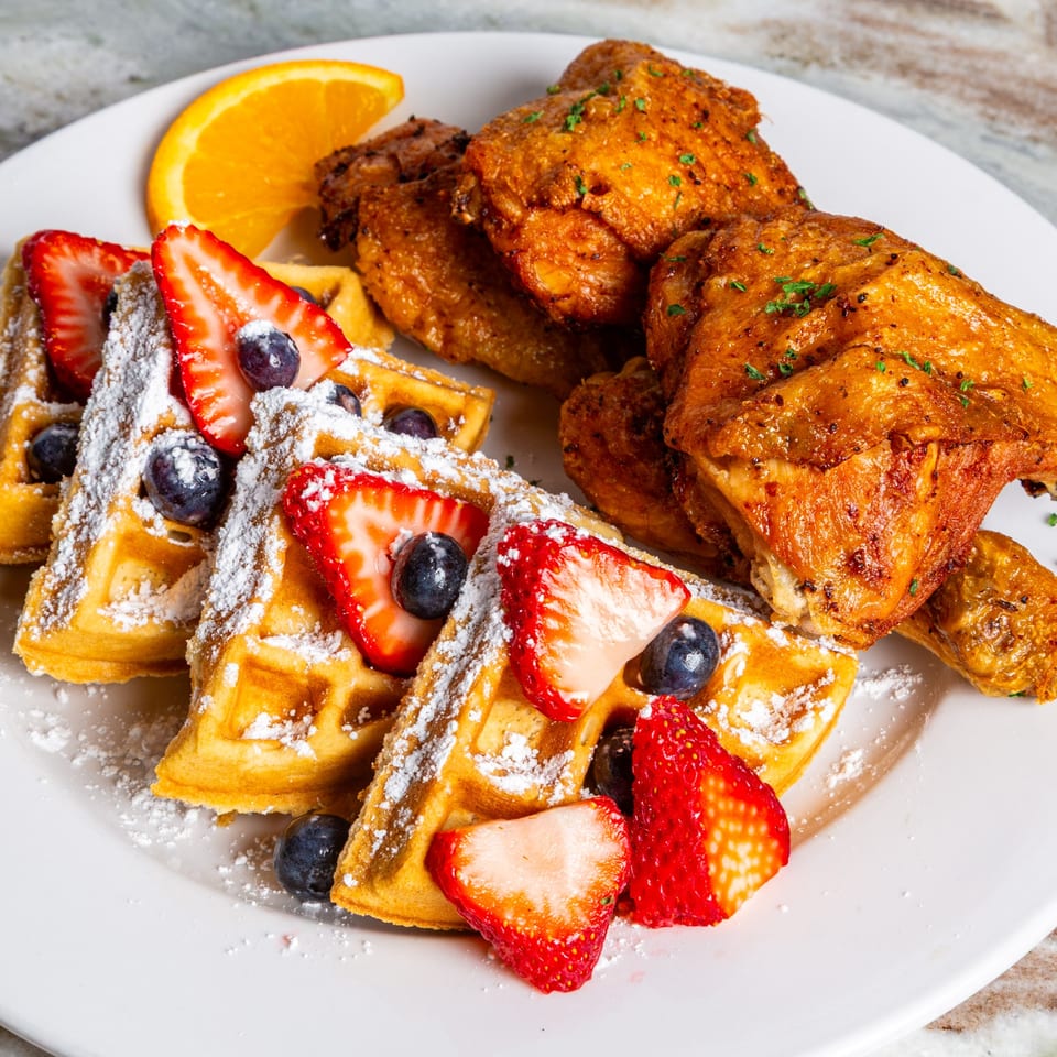 Southern fried chicken and waffles with strawberries, blueberries, powdered sugar, and an orange slice.