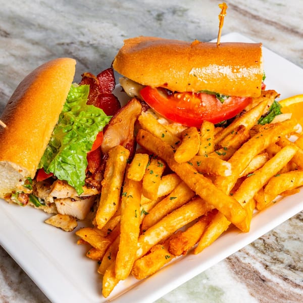 A Big John's Eatery chicken sandwich with bacon, lettuce, tomato, and fries on a white plate.