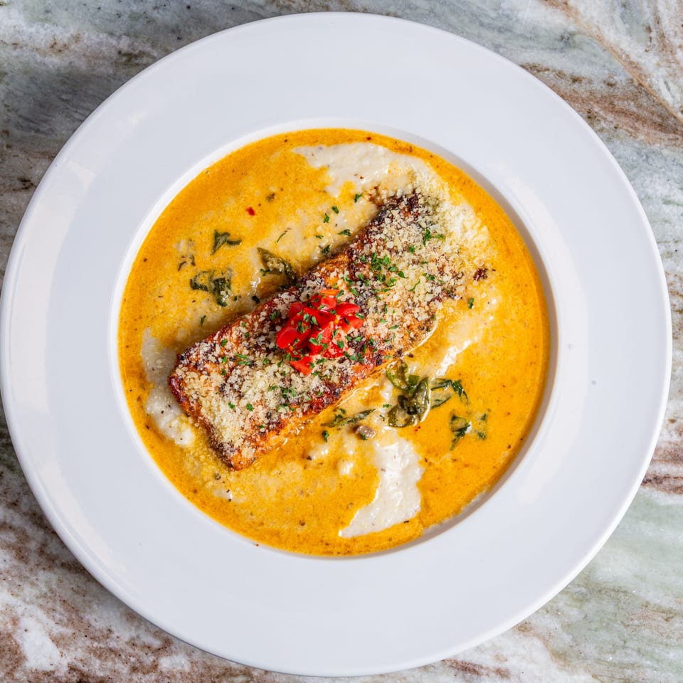 Southern-style salmon with creamy sauce, parmesan, and diced tomatoes in a white bowl.