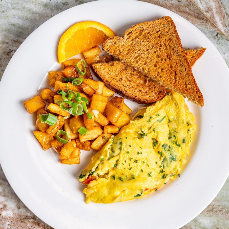 A Big John's Eatery breakfast plate with a fluffy omelet, home fries, toast, and an orange slice.